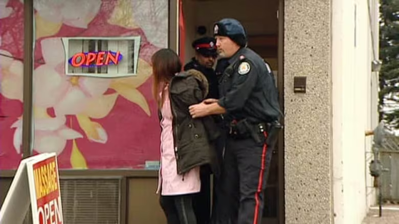 Police lead a woman out of the Lotus Flower Spa on Thursday. Police say hundreds of such massage parlours are operating in the area. PHOTO: Ivy Cuervo, CBC