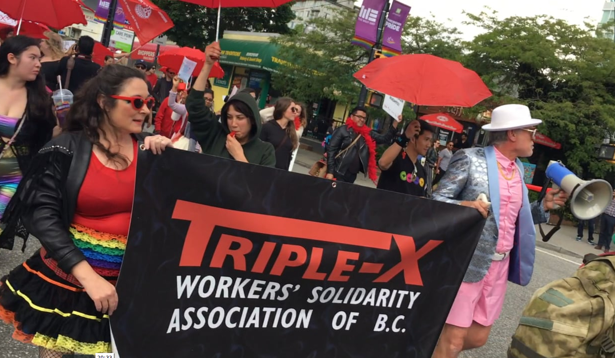 Triple-X Secretary, Kerry Porth (left) and President, Andy Sorfleet (right) lead the 7th Annual Red Umbrella March for Sex Work Solidarity up Davie Street. Vancouver, June 8, 2019. Video by Elaine Ayres